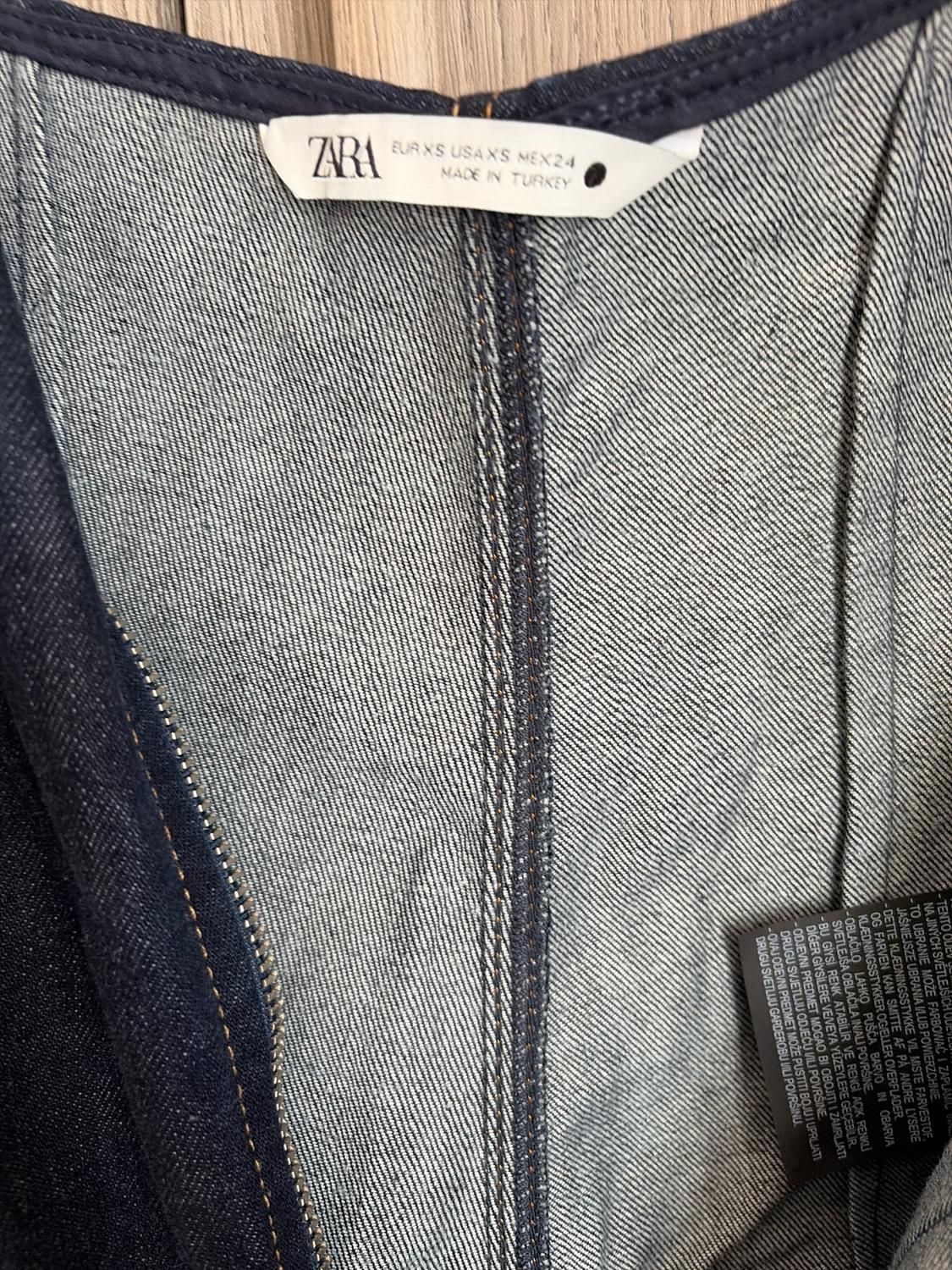 Inner label of Zara denim jeans, showing sizes EUR XS, USA XS, MEX 24, made in Turkey, on a light wooden background.