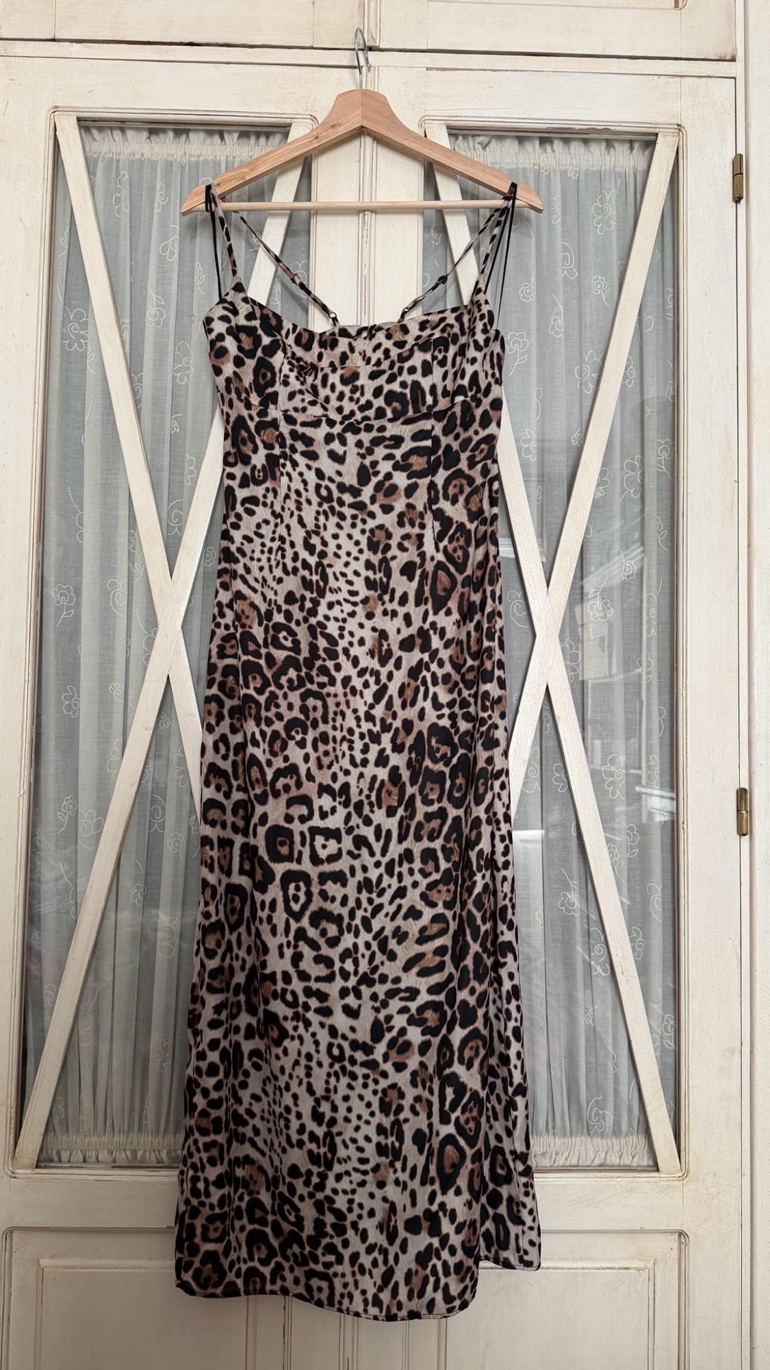Leopard print maxi dress with thin straps, hanging on a wooden hanger in front of a white door with glass panels and curtains.