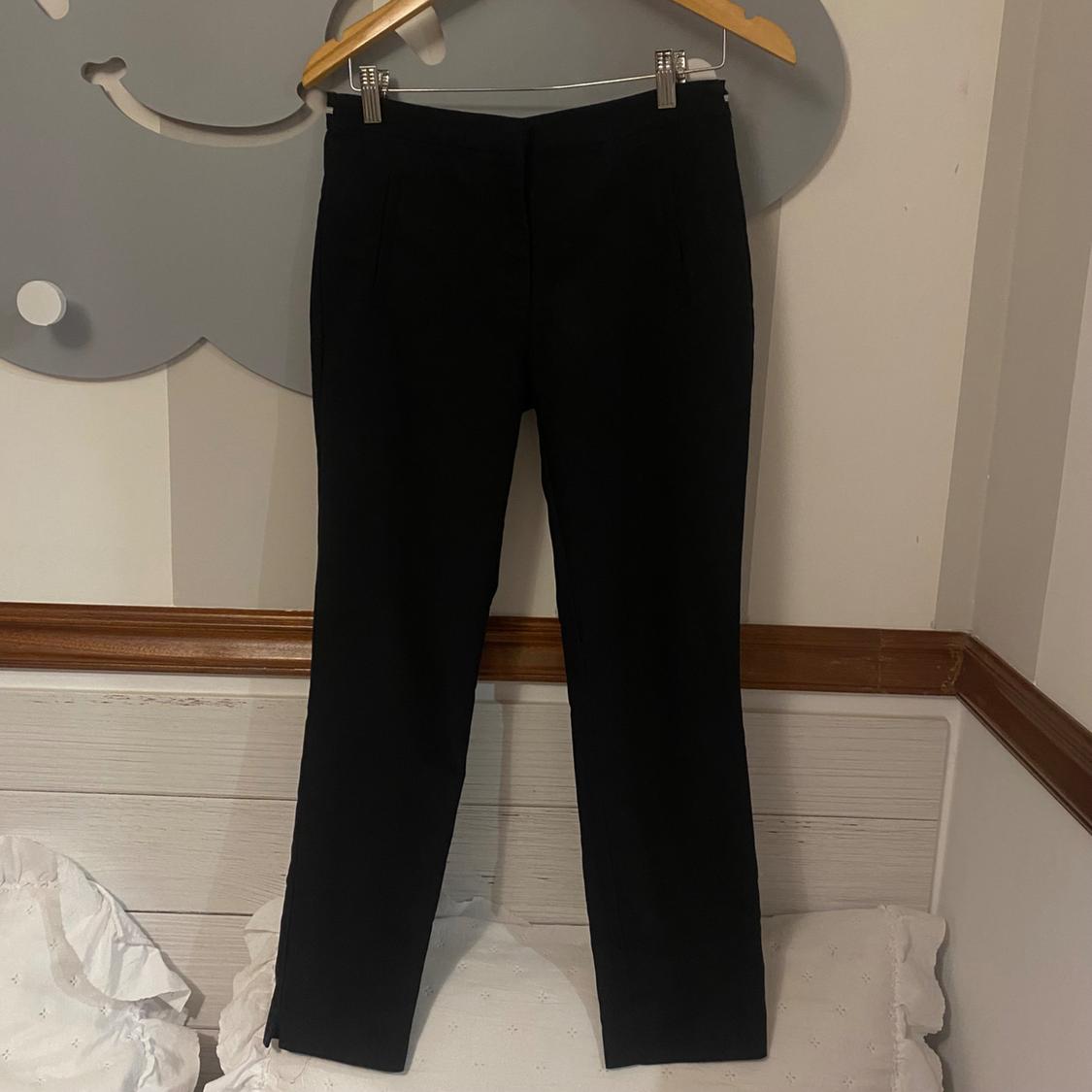 Black trousers hanging on a wooden hanger against a white wall with wooden accents and a grey decorative cloud.