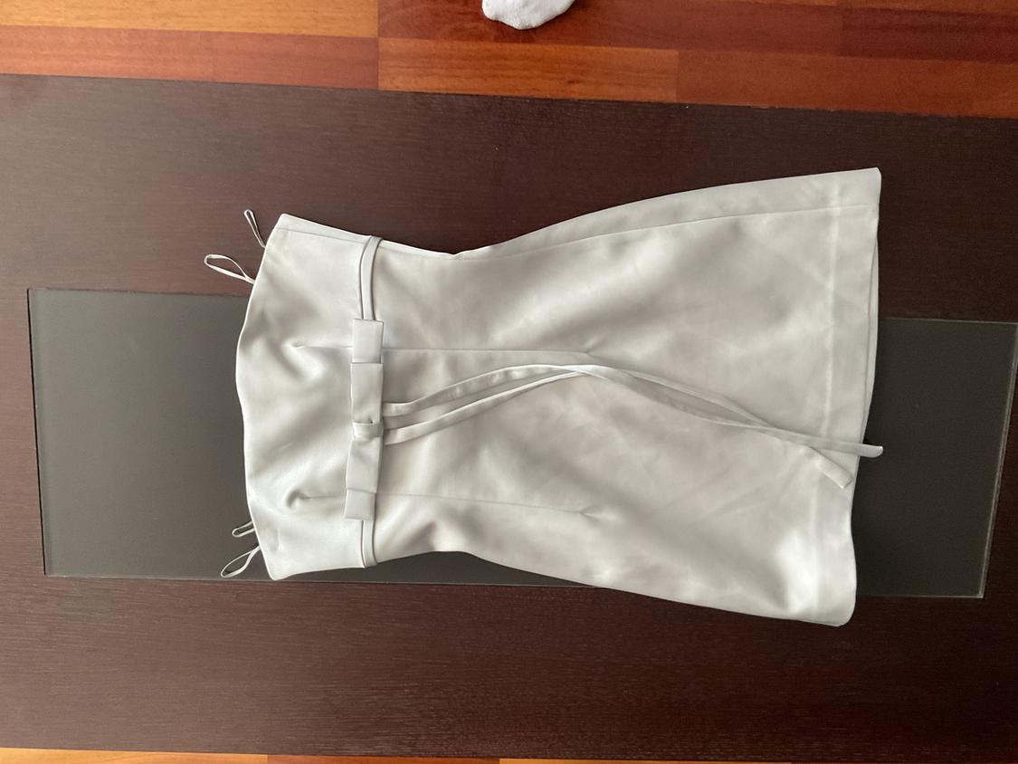 Strapless white dress with belt, placed on a dark wooden surface.