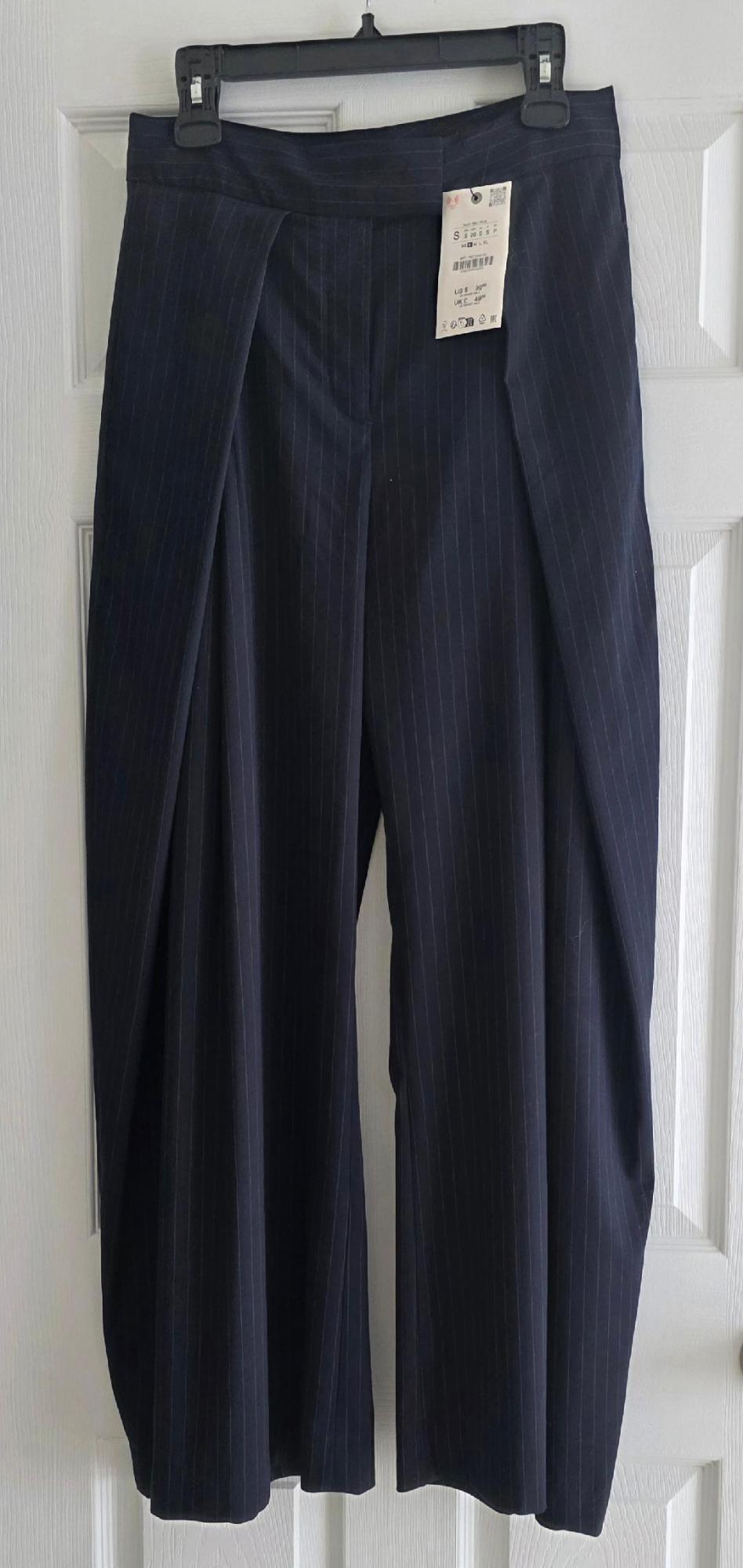 Dark trousers with vertical stripes hanging on a hanger with a visible tag, over a white door.
