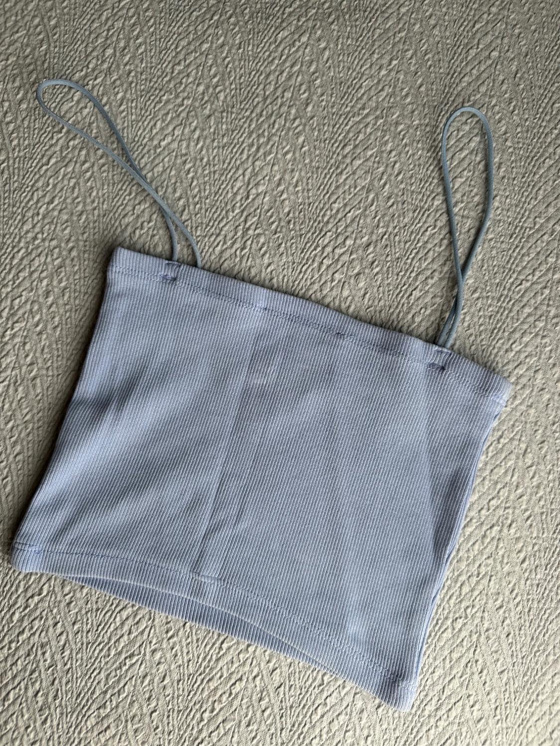 Light blue ribbed crop top with thin straps, on a light textured fabric surface in a relaxed composition.