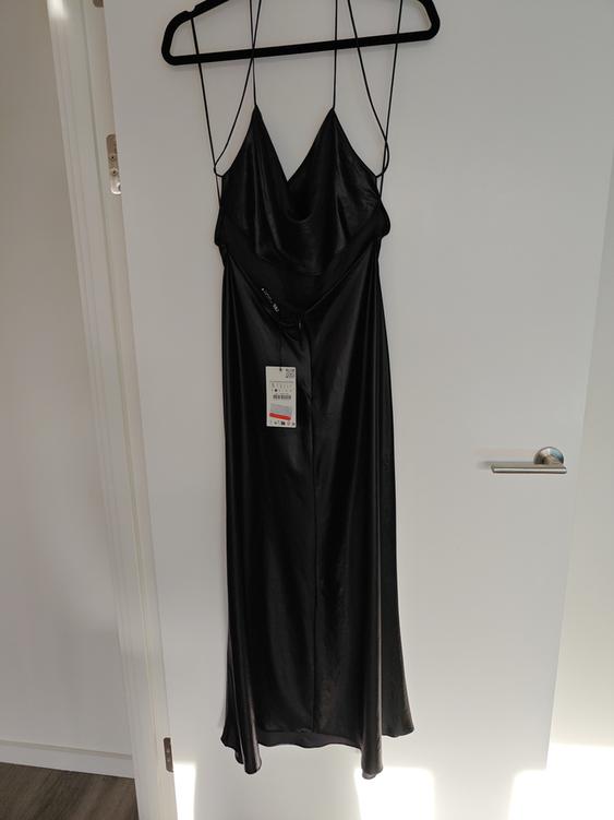 Black spaghetti strap dress hanging on a black hanger over a white door. Label visible in the centre of the dress.