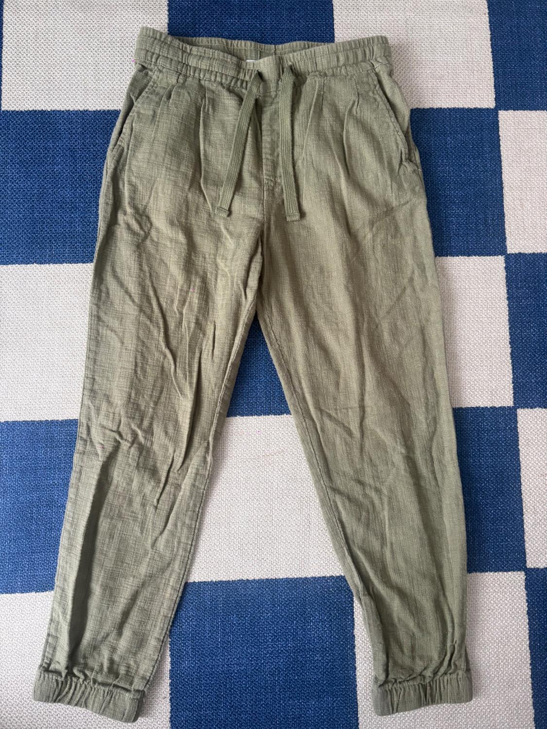 Lightweight green fabric pants with an elastic waist and drawstring, against a blue and white checkered background.