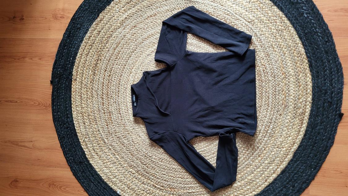 Black long-sleeved jersey on a round jute rug in beige and black tones, on a light wooden floor.