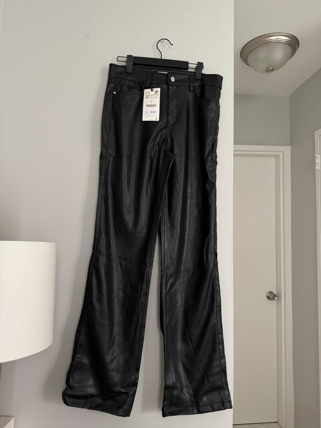 Black pants hanging on a hanger on a white wall, with a price tag visible. Minimalist room background.