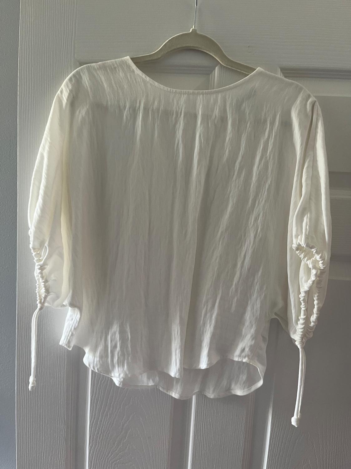 Short-sleeved white blouse with ruffles and laces, hanging on a hanger over a white door.