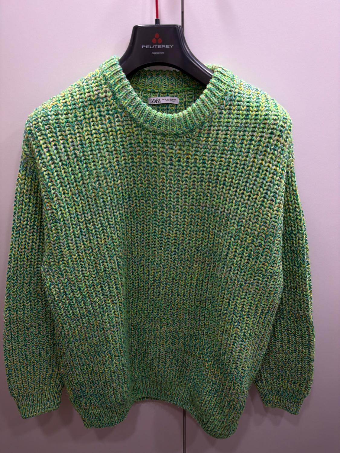Thick-textured green knitted jumper, hanging on a black Peuterey branded hanger, against a light background.