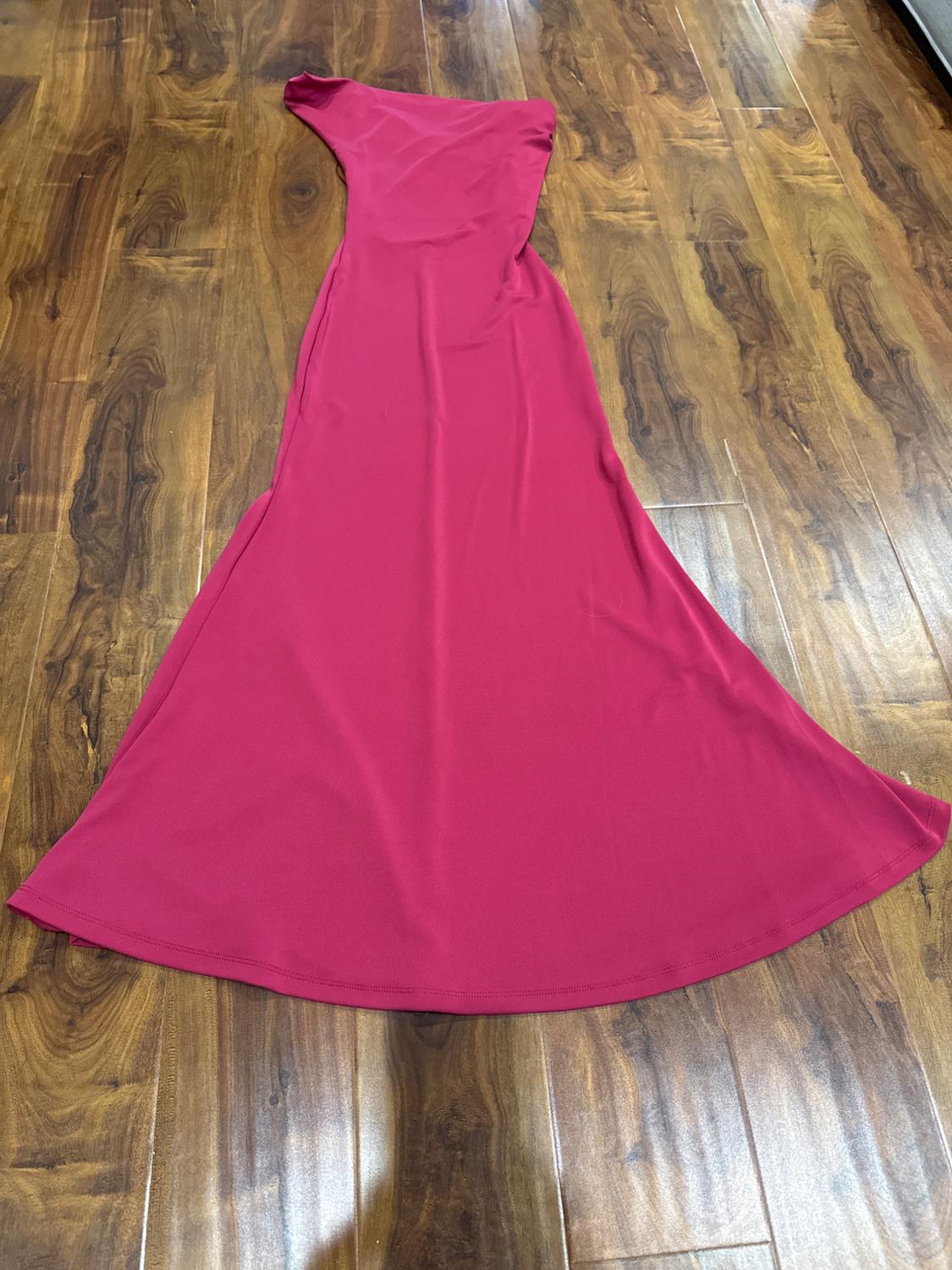 Long fuchsia dress with an asymmetrical one-shoulder design, sleeveless, laid out on a wooden floor.