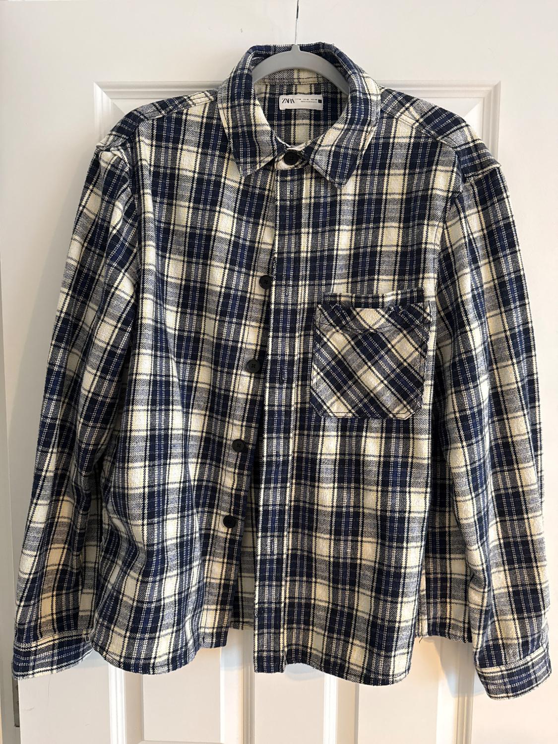 Blue and white checked shirt hanging on a hanger, with a chest pocket and dark buttons.