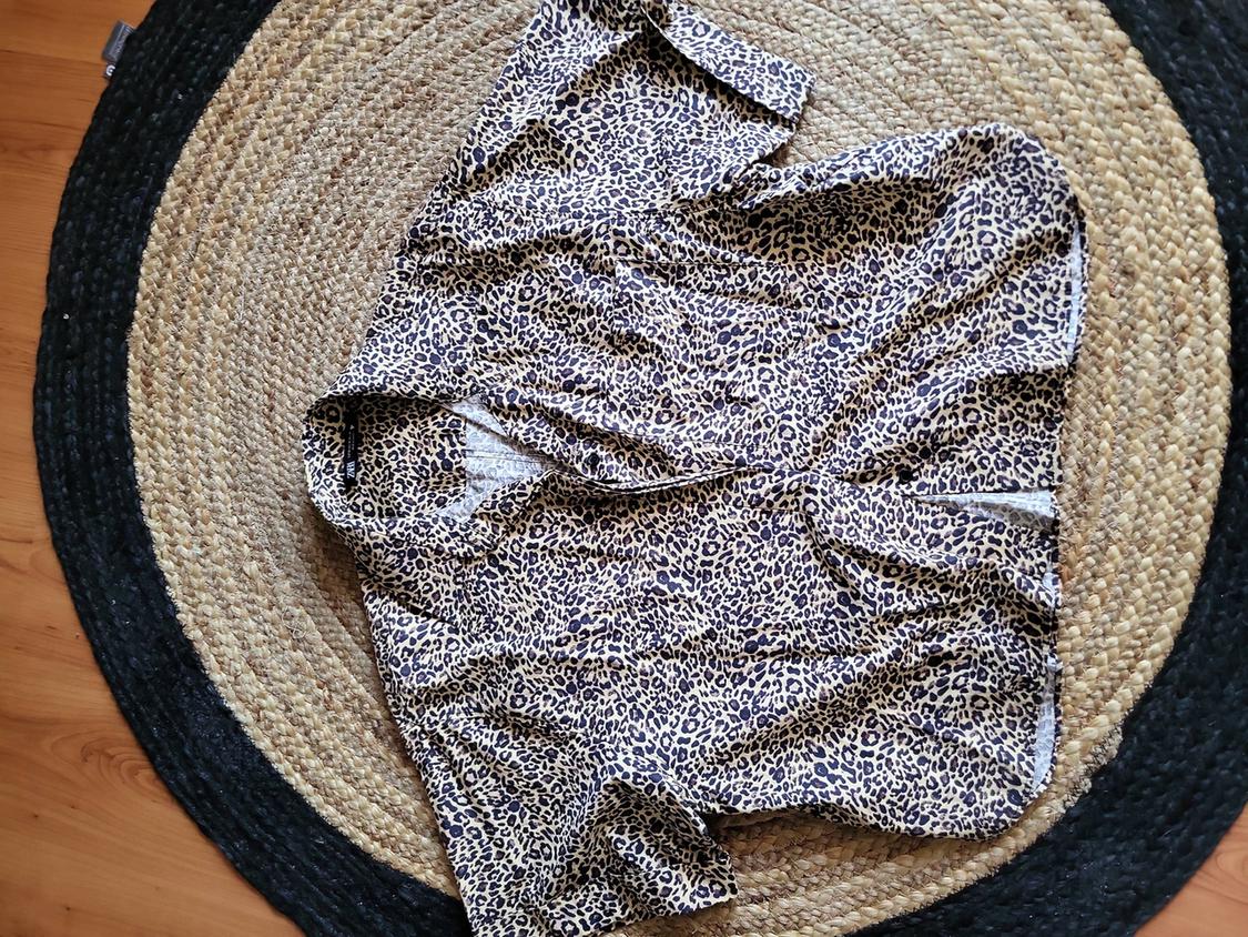 Πουκάμισο με animal print πάνω σε μια στρογγυλή ψάθινη χαλί από γιούτα σε αποχρώσεις του μπεζ και του μαύρου, τοποθετημένο σε ένα ανοιχτόχρωμο ξύλινο πάτωμα.