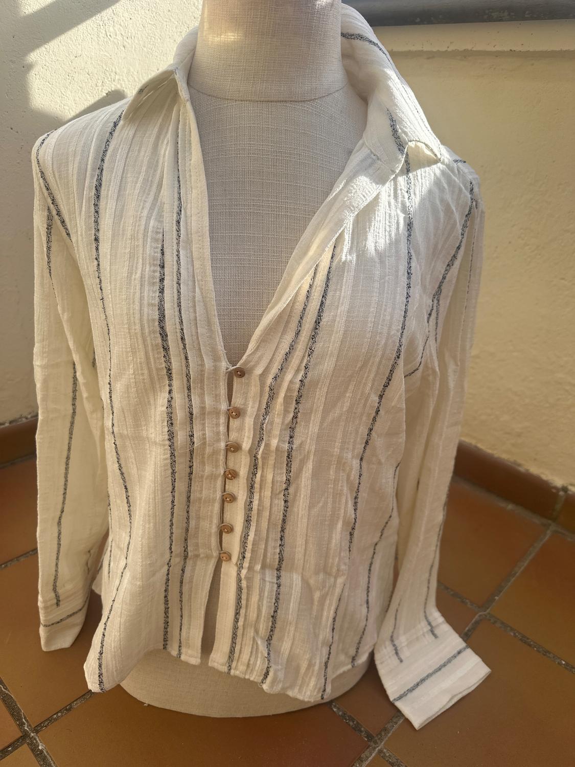 White shirt with black stripes and brown buttons on a mannequin, lit by natural light on a brown tiled floor.