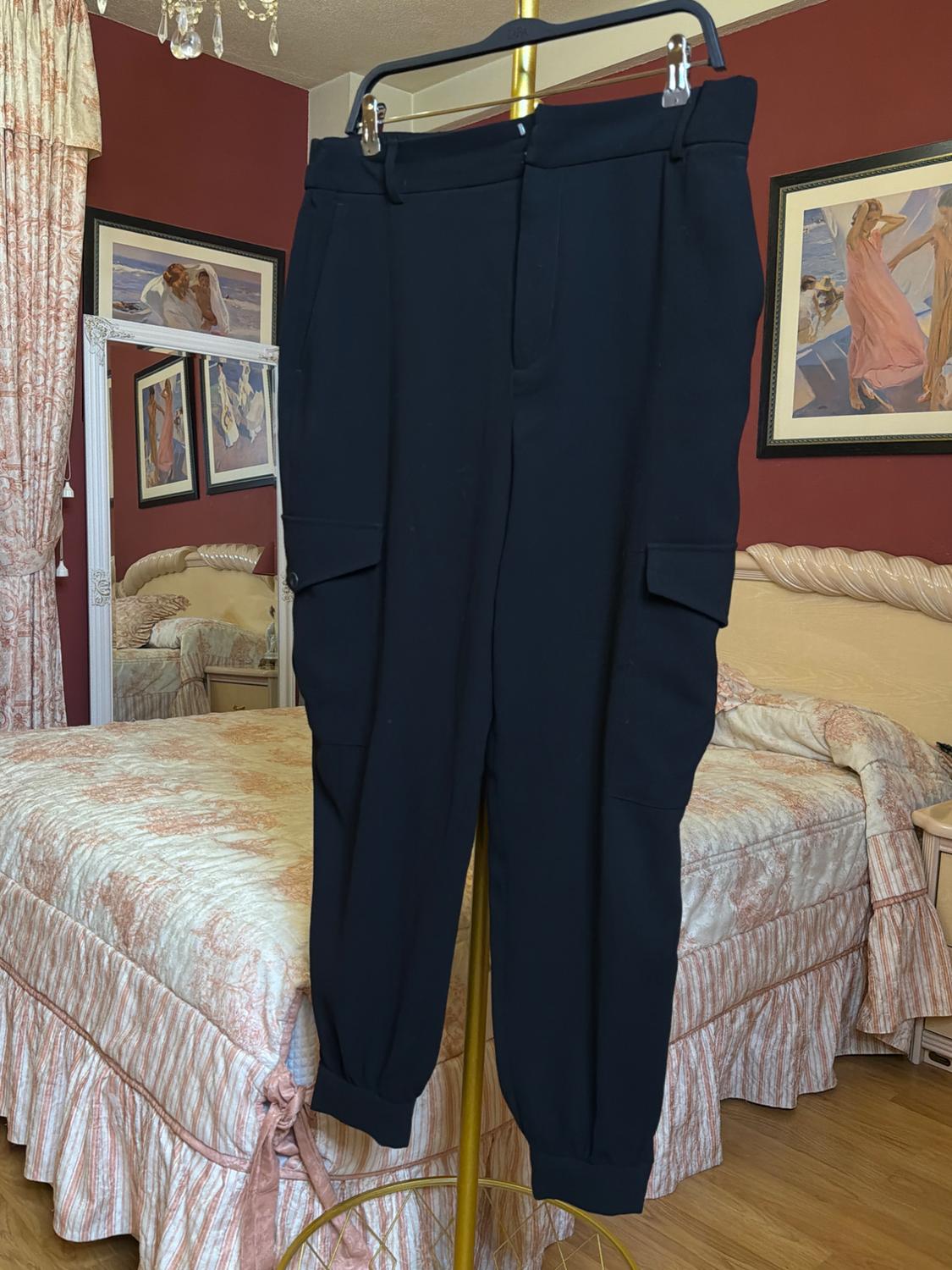 Black trousers hanging on a gold hanger in a bedroom with red walls, a bed with a patterned bedspread, and pictures on the wall.