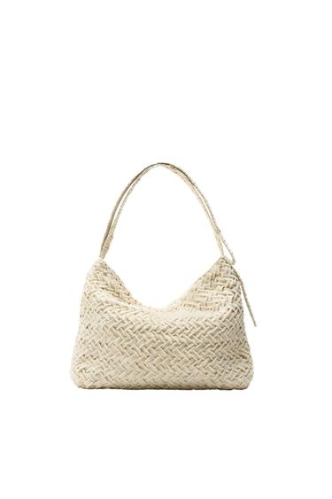 Beige knitted bag with a short handle, on a white background. Interwoven pattern design visible across the entire surface.
