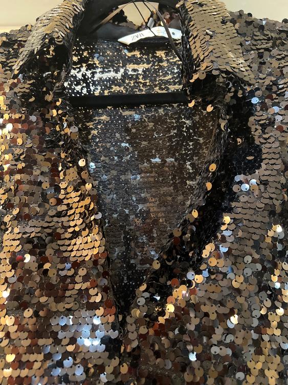 Gold and black sequined shirt hanging on a hanger, with visible tag on the collar.