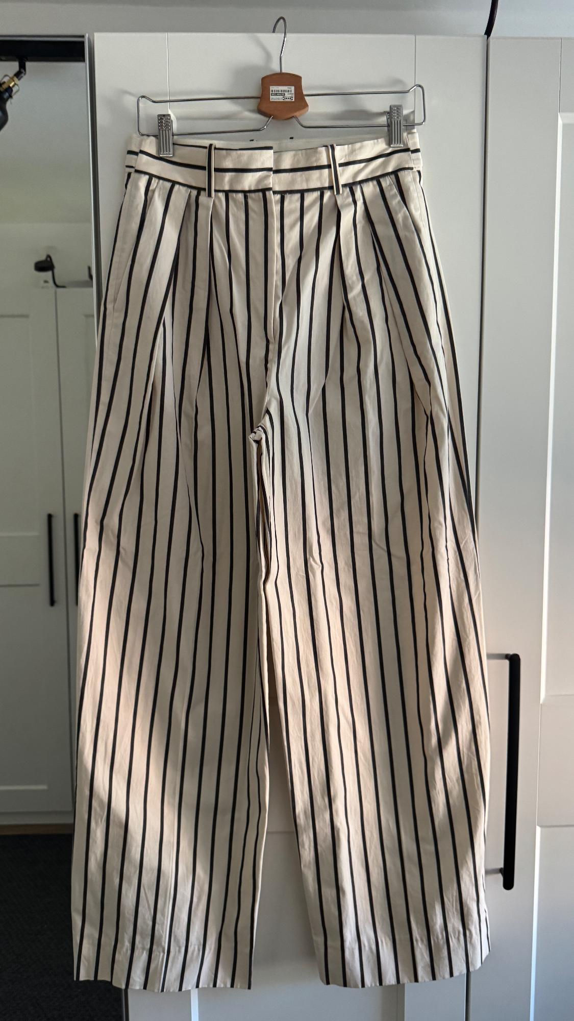 Black and white vertical striped trousers hanging on a wooden hanger, white wardrobe background.