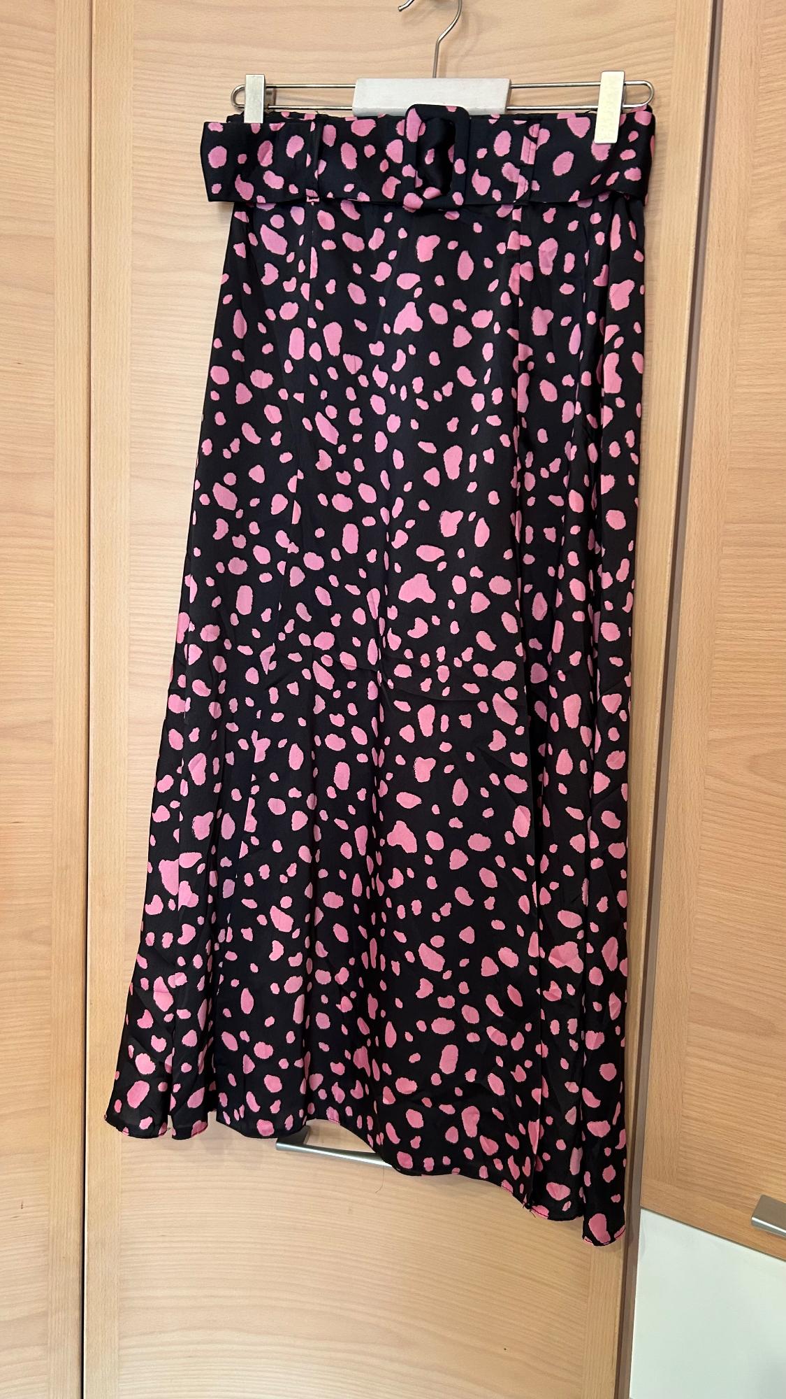 Black skirt with a pink spot print, hanging on a light wooden hanger against a background of wooden wardrobe doors.