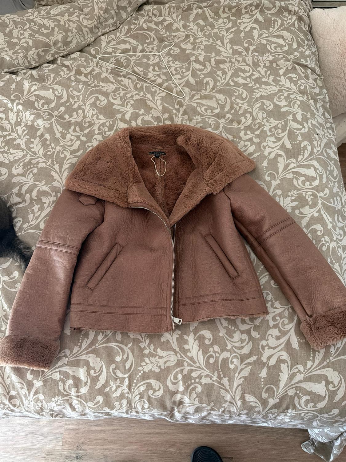 Brown aviator-style jacket with a fur collar and cuffs, placed on a bed with a beige floral-print bedspread.