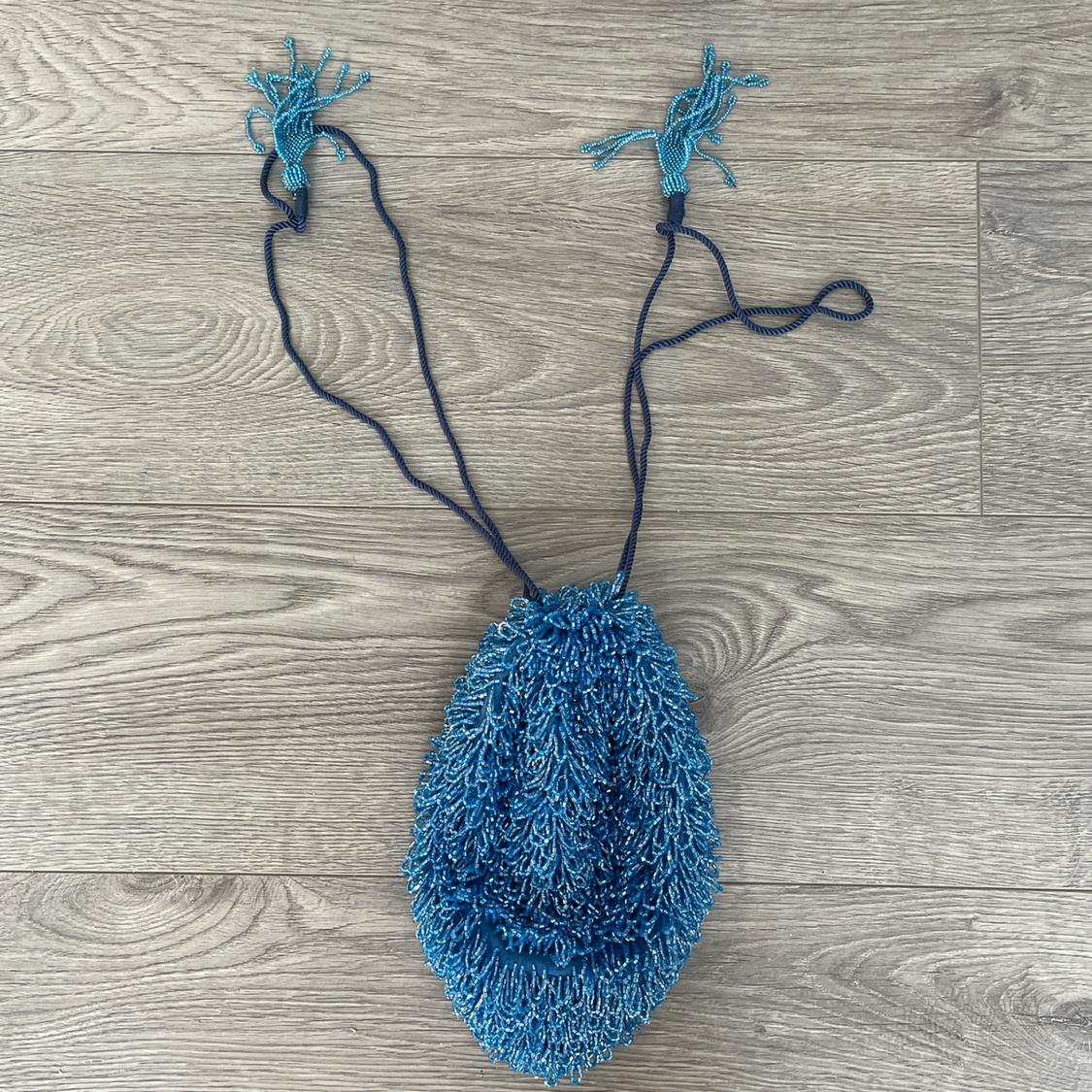 Blue beaded bag with drawstrings and tassels on a grey wooden floor. Textured and vibrant design.