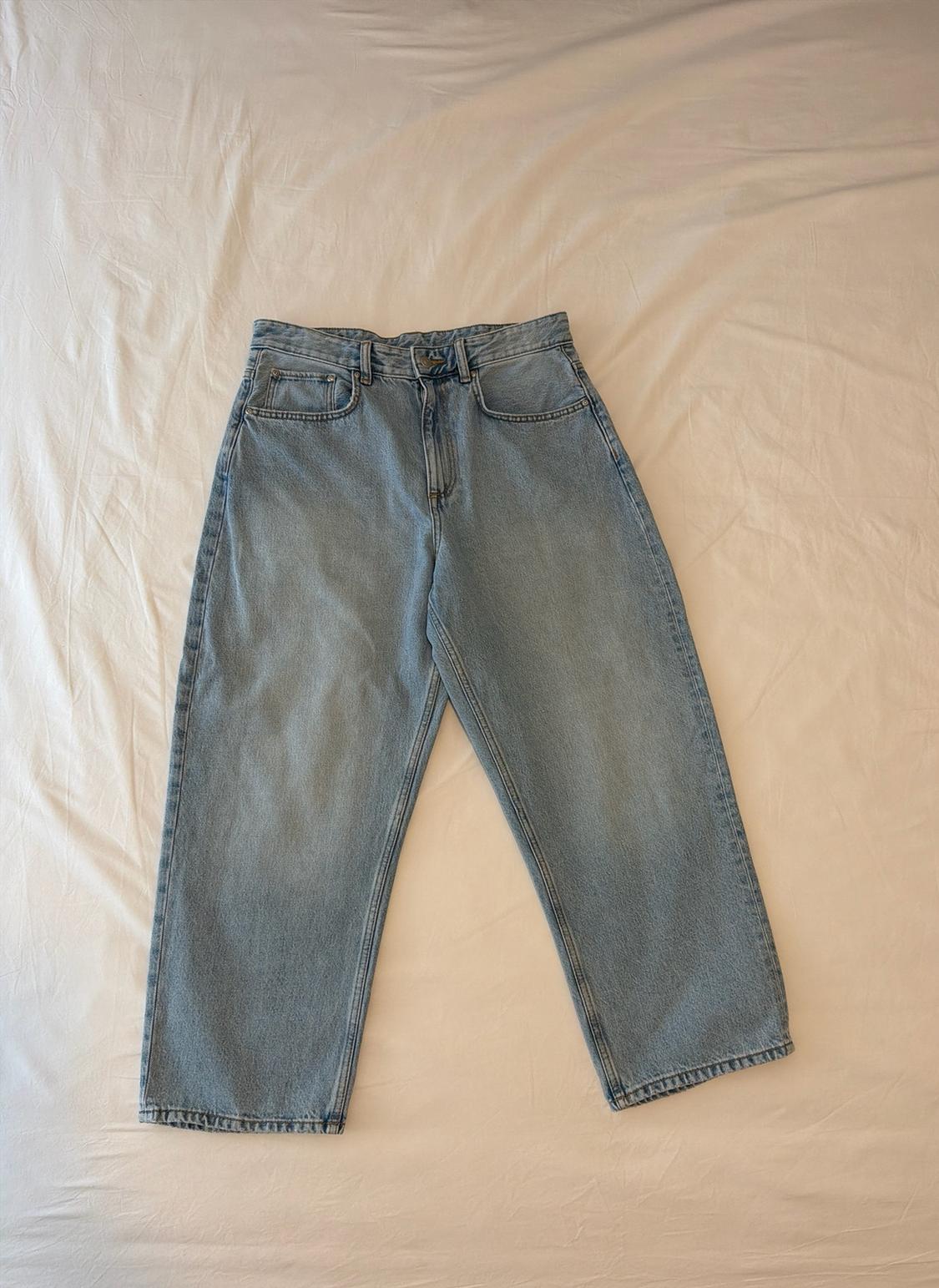 Light blue loose-fit jeans, photographed on a crumpled white sheet. Casual and relaxed style.