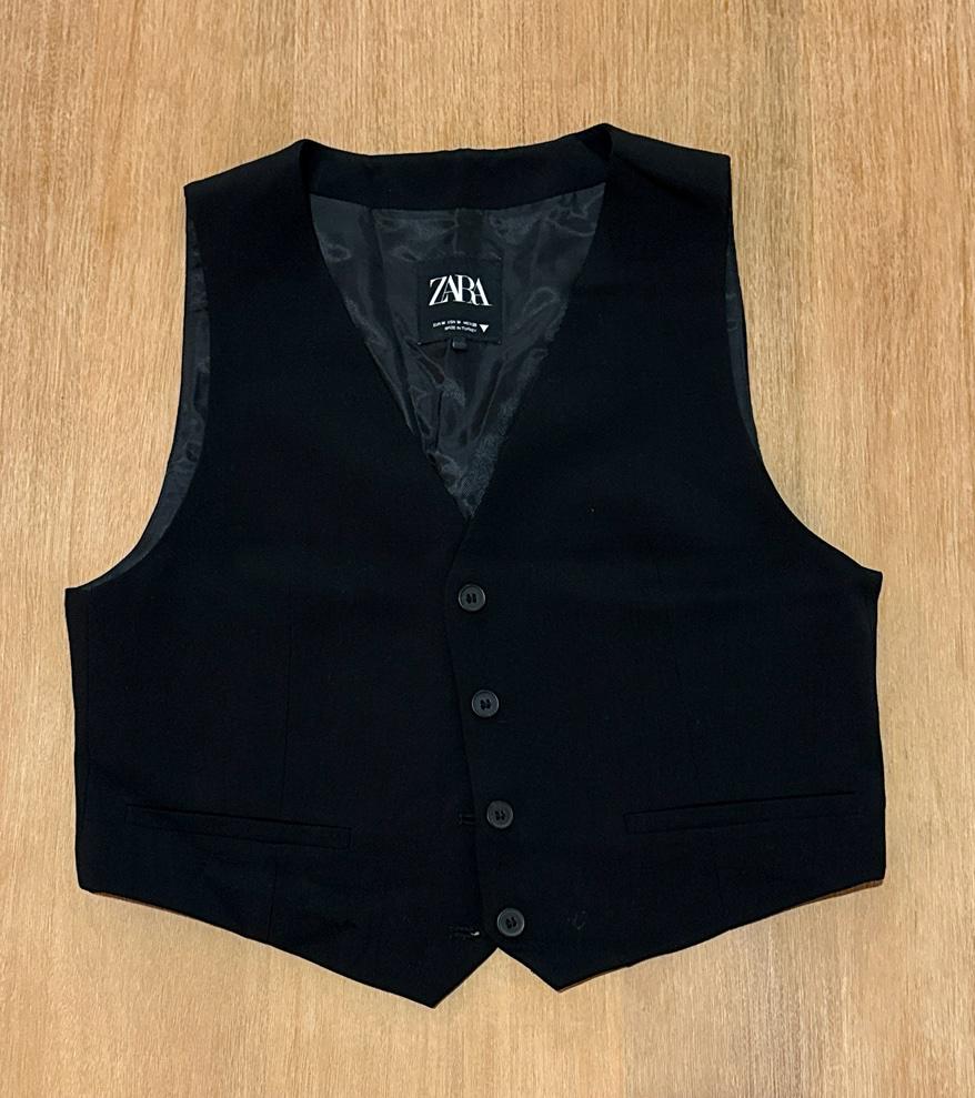Black vest with button closure and front pockets on a wooden background. The interior label reads ZARA.