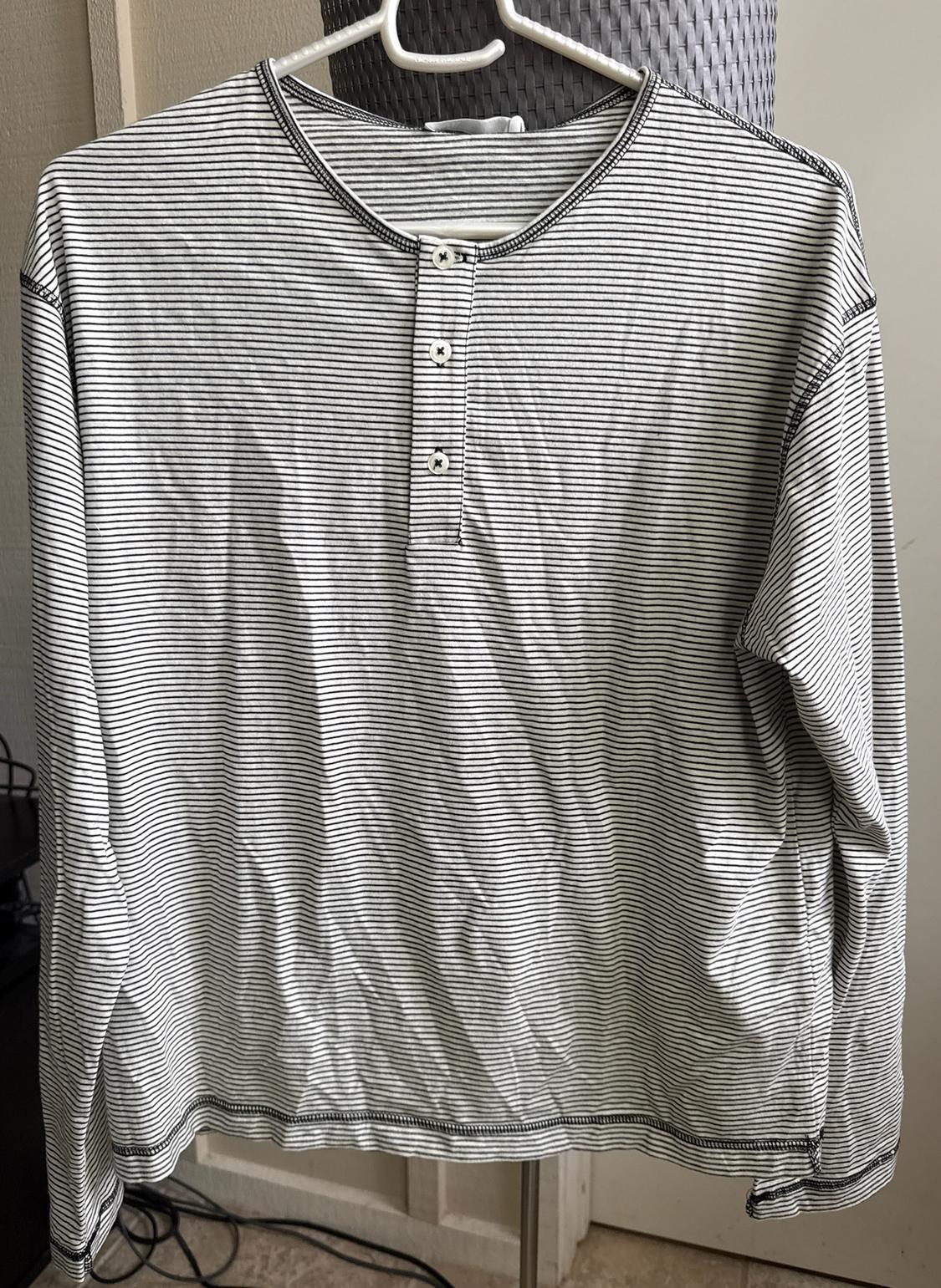 White long-sleeved T-shirt with thin horizontal black stripes and three buttons at the front, hanging on a white hanger.
