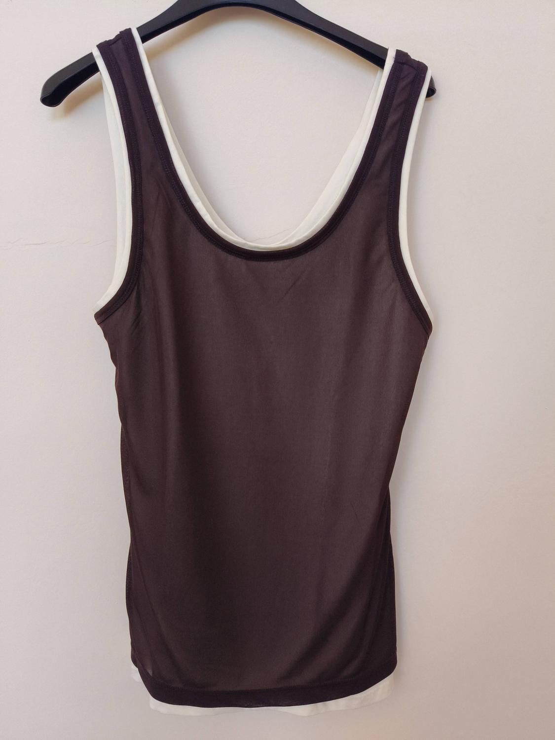 Dark brown vest over a white t-shirt, hanging on a black hanger in front of a light-coloured wall.