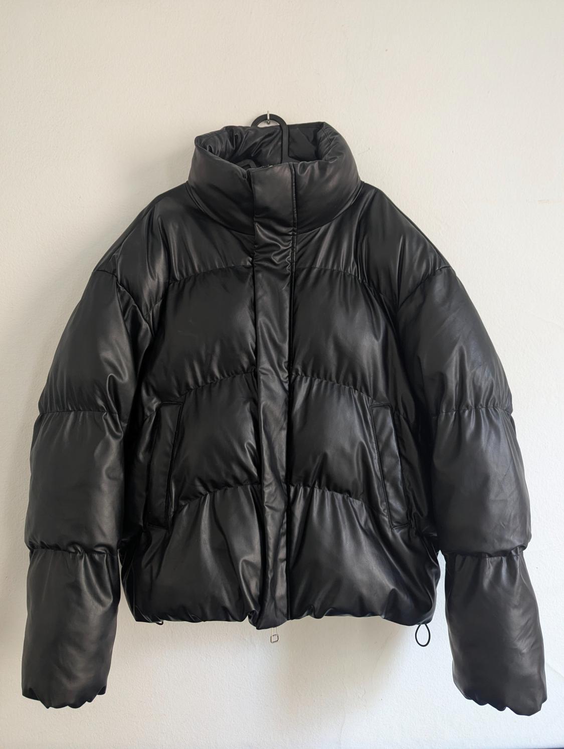 Black padded jacket hanging on a hanger against a white wall. High neck design with long sleeves.