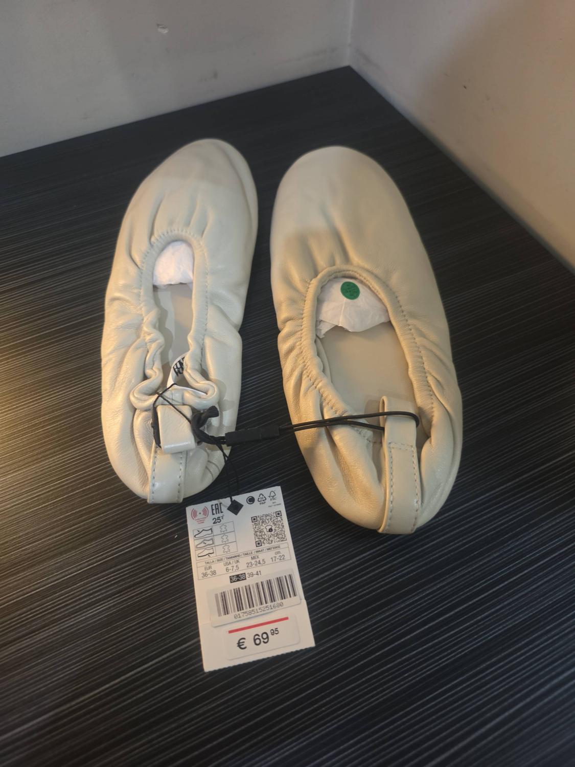 Cream gathered ballet pumps on a dark background. Label: EAC 25 EUR 36-38 USA/UK 6-7.5 MEX 23-24.5 36-38 39-41 01758515251680 € 69.95.