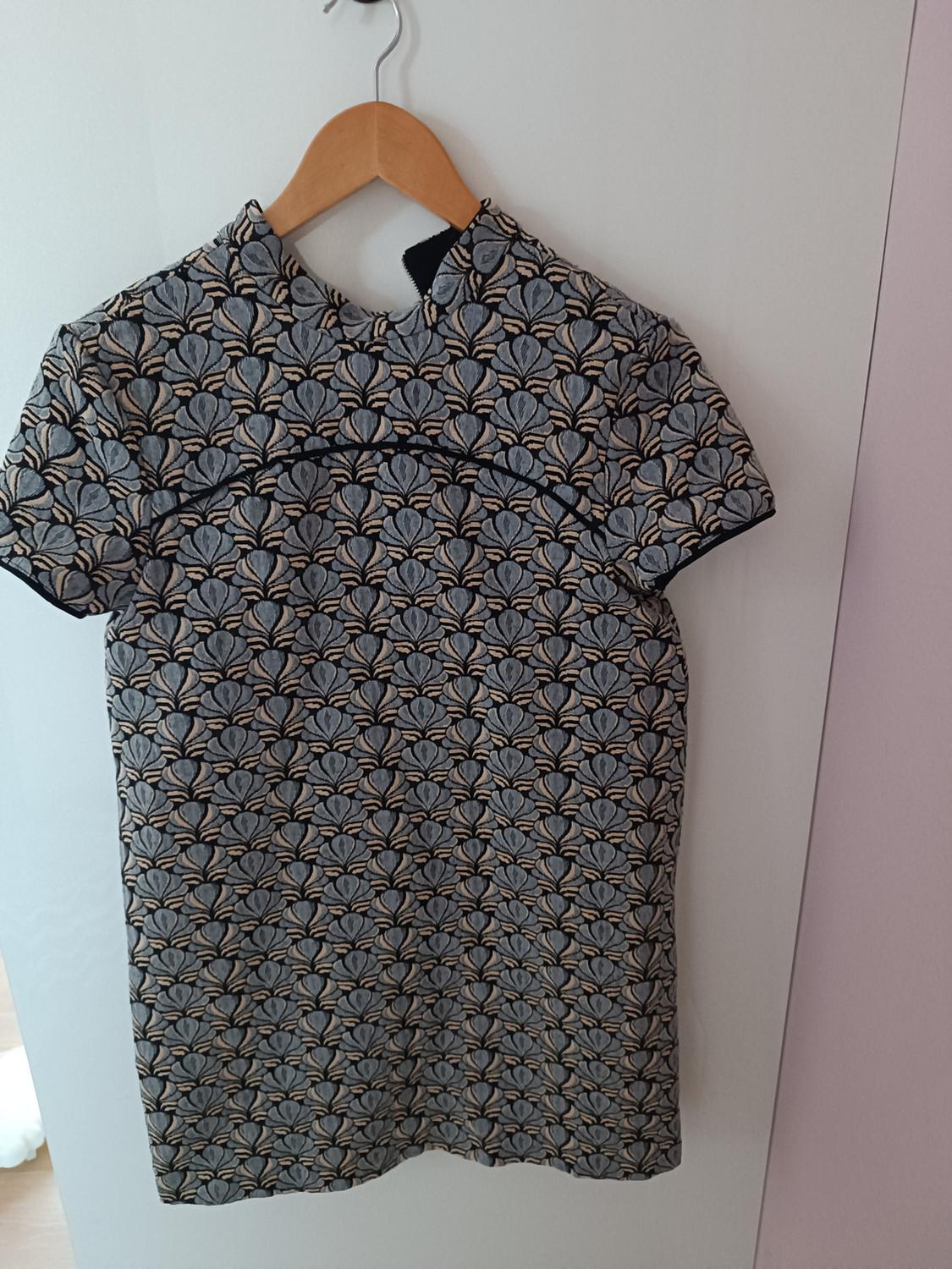 Dress hanging on a wooden coat hanger, with a geometric print in shades of grey and black, on a white background.