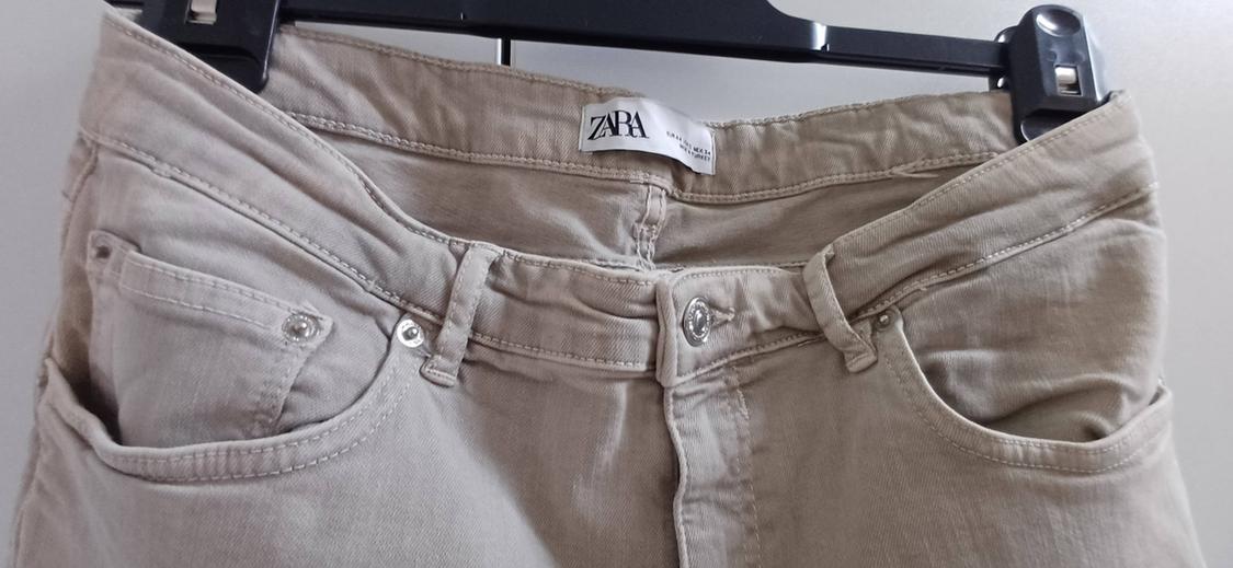 Beige trousers hanging on a black hanger, with a visible Zara label on the waistband.