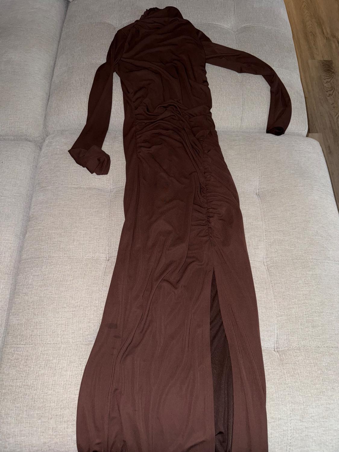 Long-sleeved brown dress with ruching and a slit at the bottom, spread out on a beige sofa.