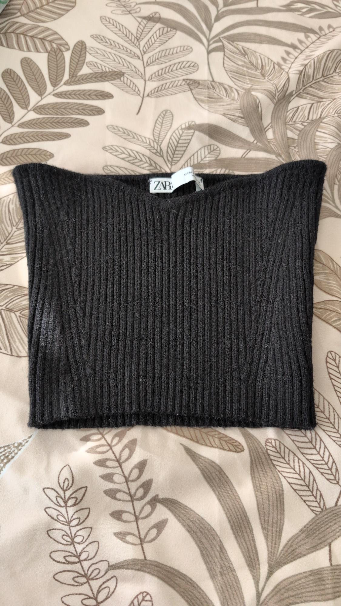 Black ribbed strapless top with the ZARA label, photographed on a fabric with a beige leaf print.