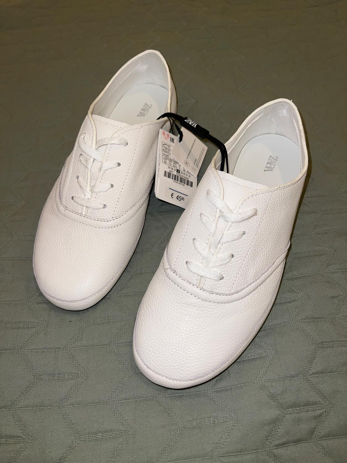 White lace-up shoes on textured green fabric. Casual style. Visible text: ZARA, EAC, € 45.95.