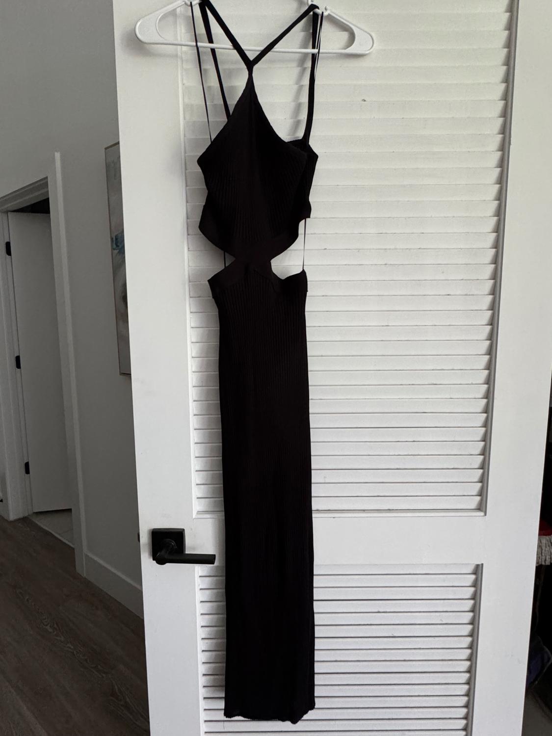 Long black dress with spaghetti straps and a side slit design, hanging on a white door with blinds.