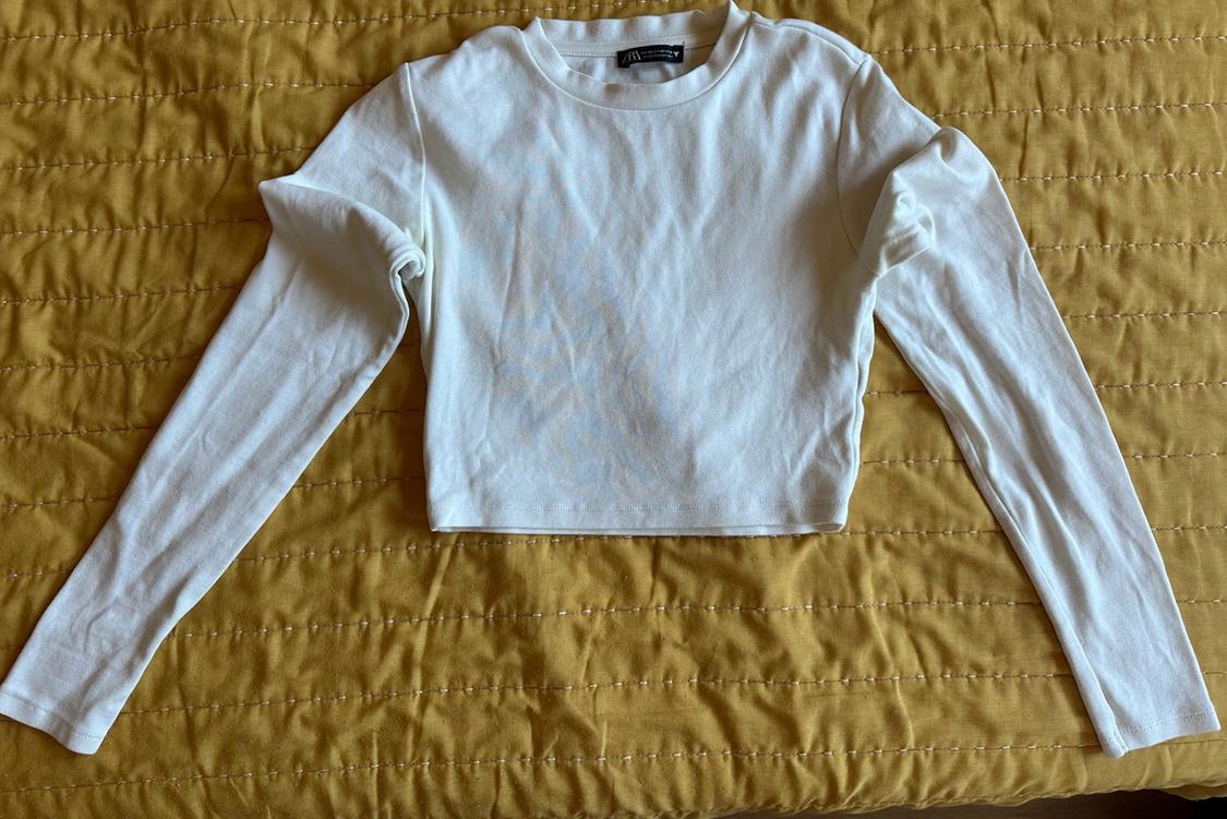 White long-sleeved cropped T-shirt laid out on a textured mustard-yellow bedspread.