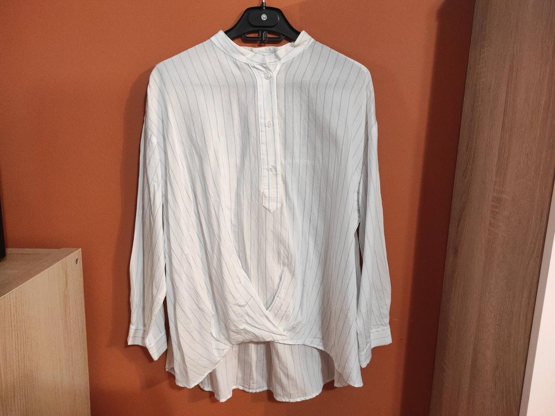 White shirt with thin vertical stripes, hung on a black hanger, against an orange background and next to a light wood cabinet.