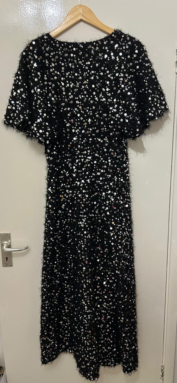 Black sequin dress hanging on a wooden hanger over a white door.