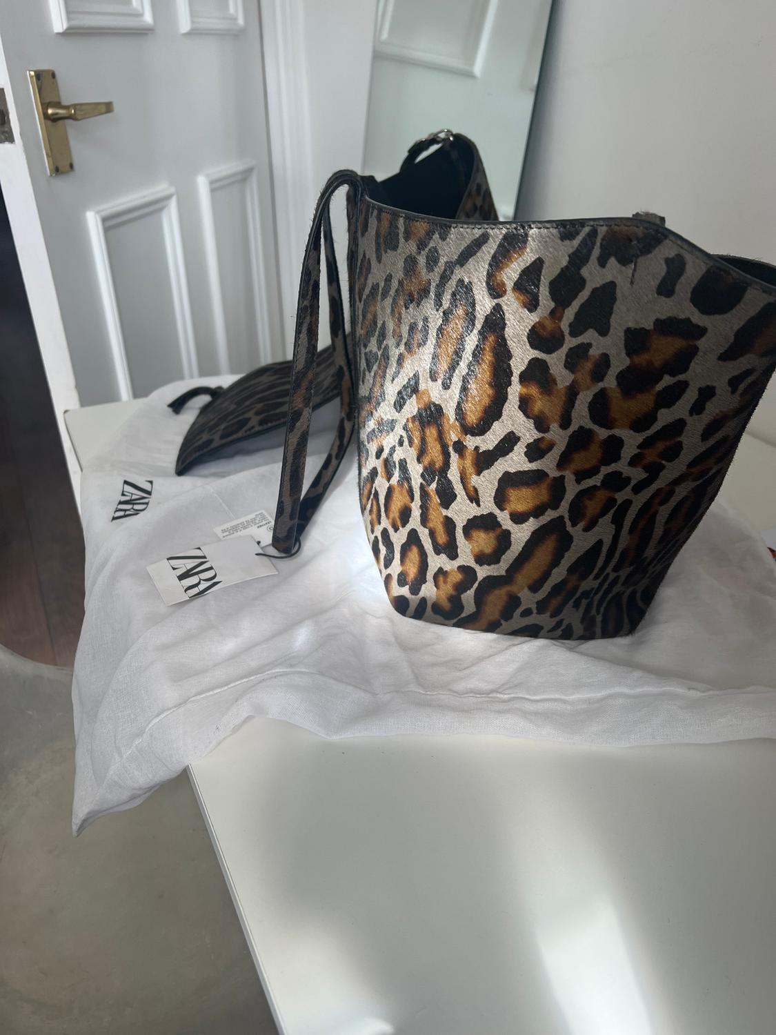 Leopard print handbag on a white table, next to a white fabric bag with the "ZARA" brand visible.