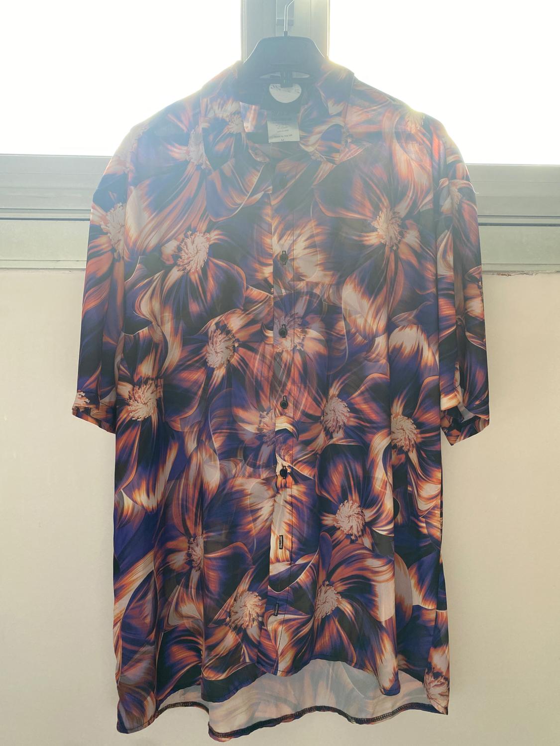 Front view of a shirt with an orange and purple floral print, central buttons, short sleeves.