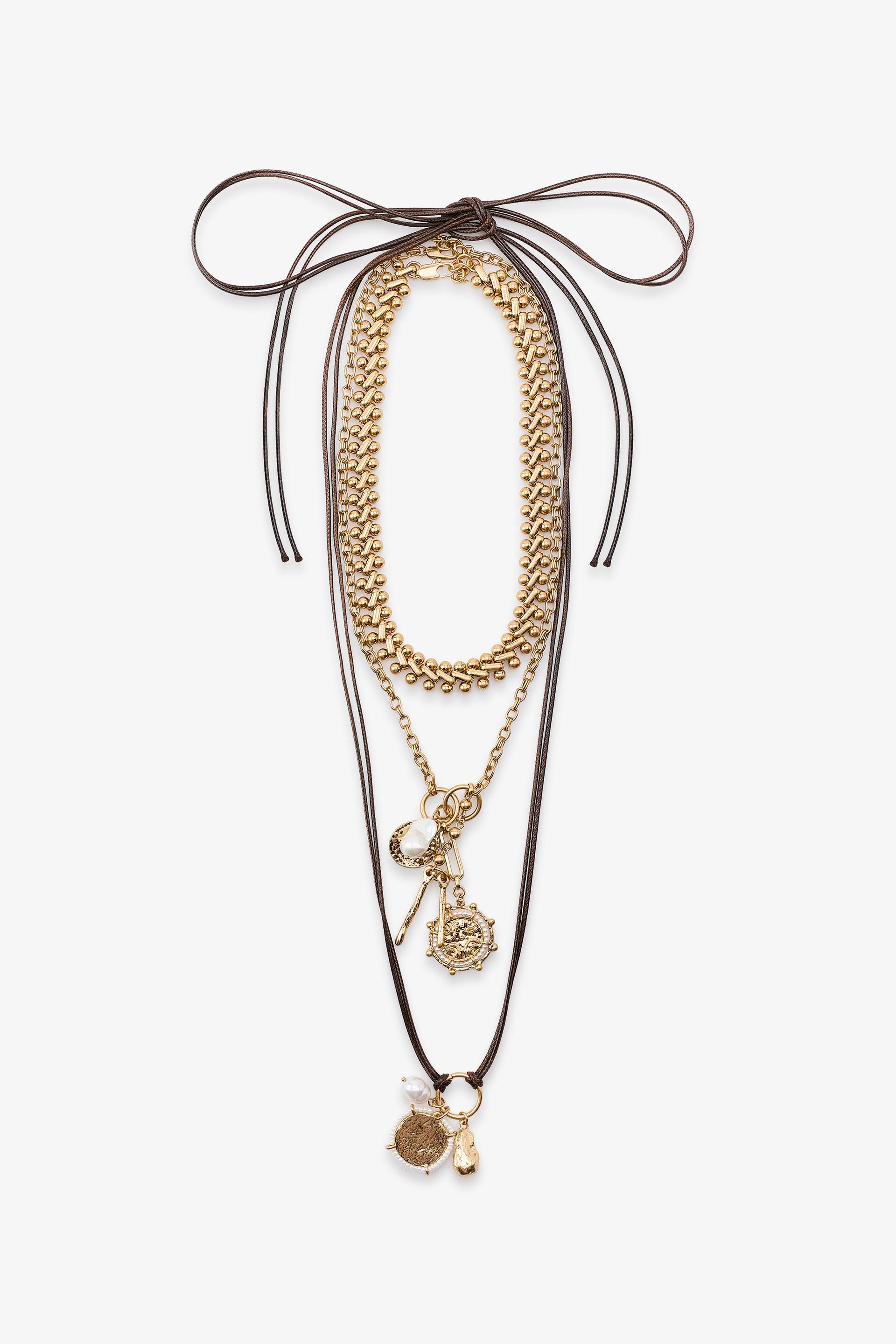 Σετ τριών χρυσών κολιέ: αλυσίδα με charms, κορδόνι με κόμπους και κρεμαστά στοιχεία, και μεταλλικοί κρίκοι.