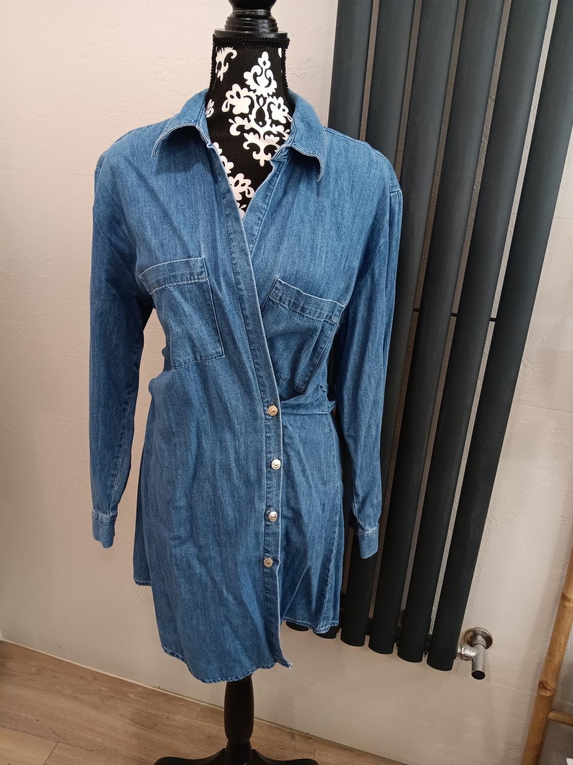 Blue denim shirt dress on a mannequin with a white wall and black radiator in the background.