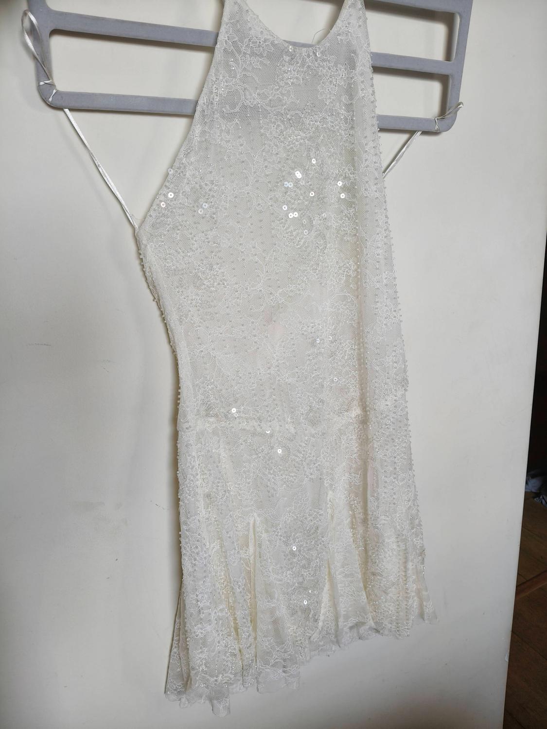 Short white lace and sequin dress with a halter neck, hanging on a grey hanger against a white background.