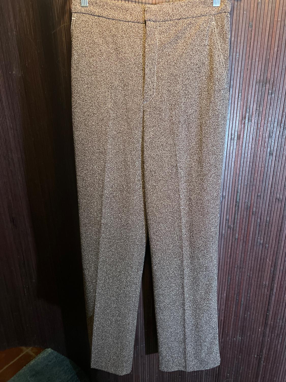Brown pants hanging on a dark wood wall. The fabric texture is visible, creating a speckled effect.