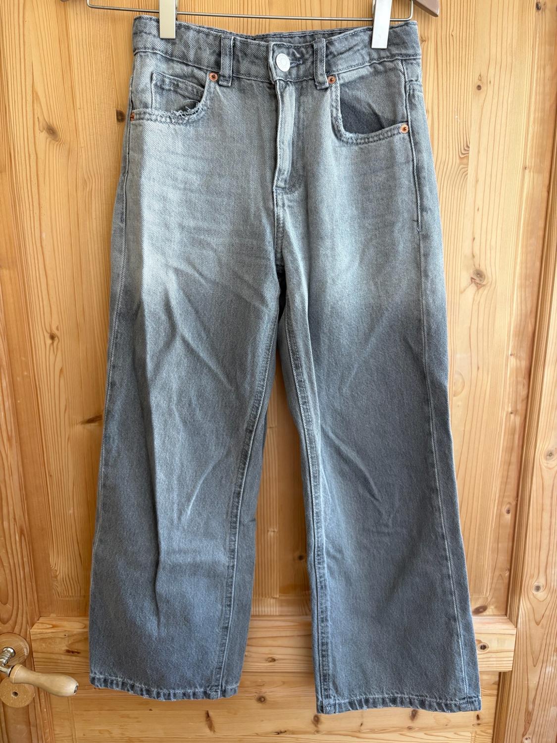 Grey distressed-wash jeans hanging on a hanger on a light wood door. Casual and relaxed style.