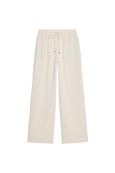 Front view of beige trousers with elasticated waistband and drawstring.