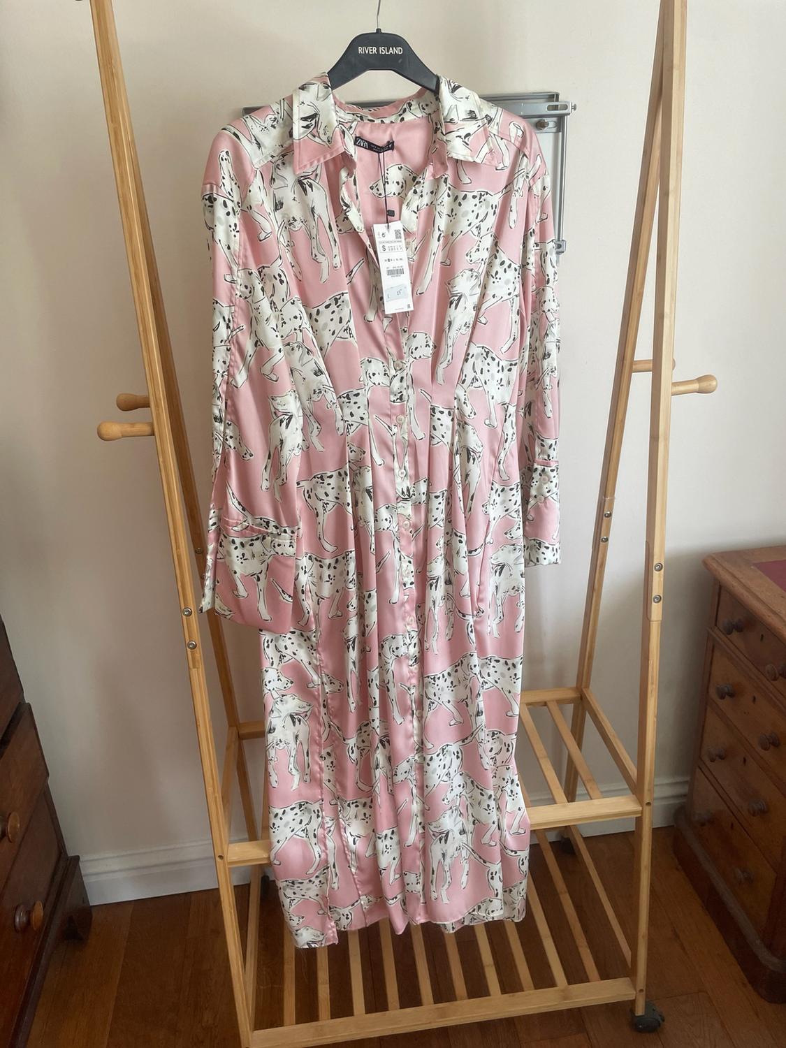 Pink maxi dress with a dalmatian print hanging on a wooden clothes rack. Black hanger with the text RIVER ISLAND.