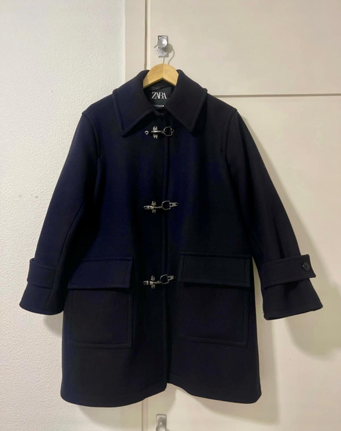 Front view of black coat with ring closures and large pockets.
