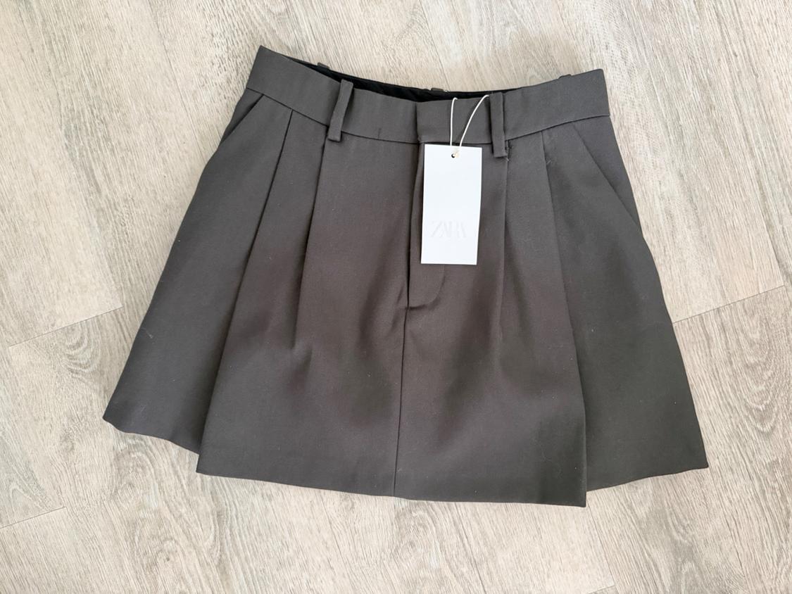 Short grey pleated skirt with a waistband, visible hang tag. Light wood background.