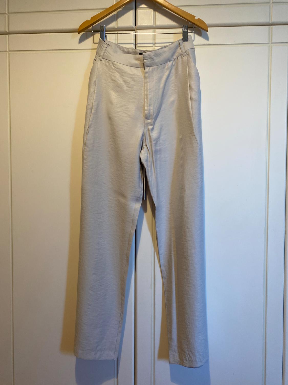 Beige trousers hanging on a wooden hanger over a white door. Simple and classic style, with side pockets.